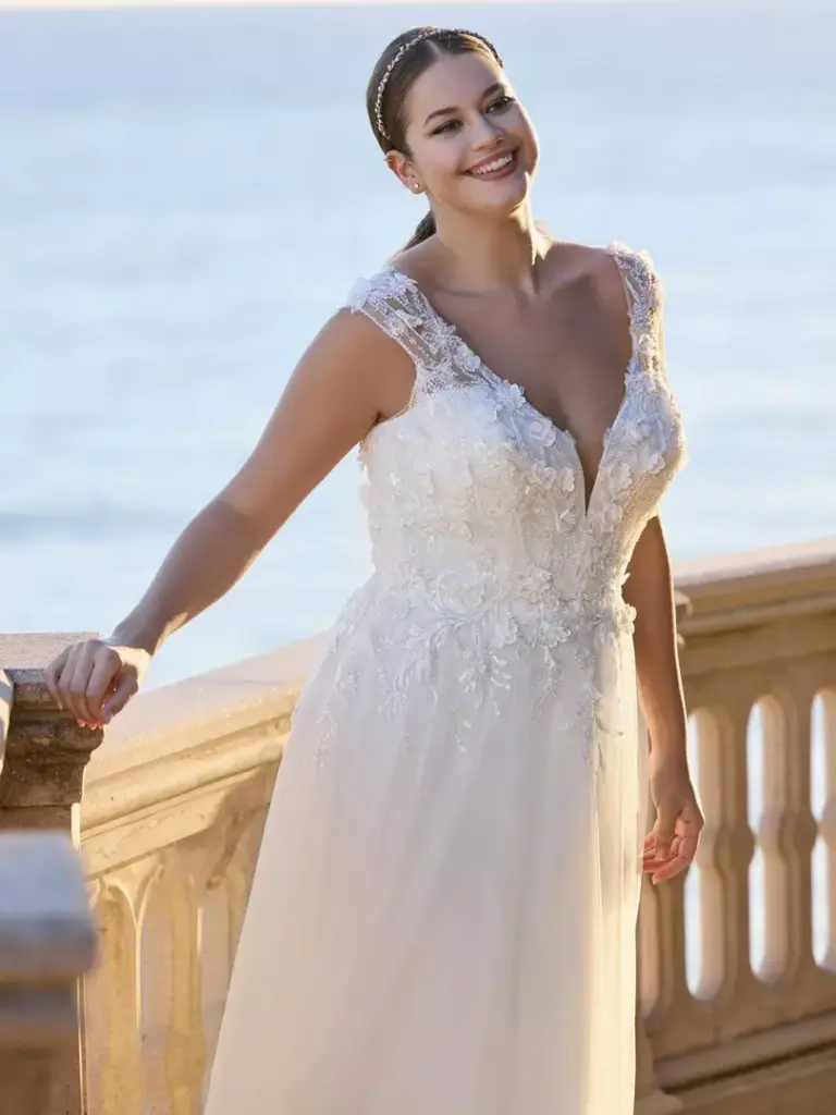Brautkleid mit V-Ausschnitt, breiten Trägern und floraler Spitze an einer Balustrade