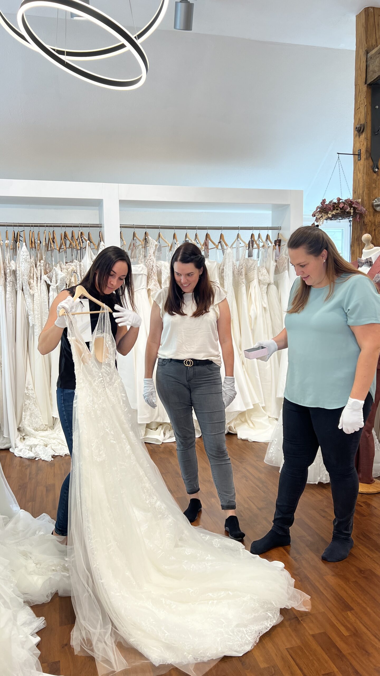 Drei Frauen betrachten ein Brautkleid mit langer Schleppe