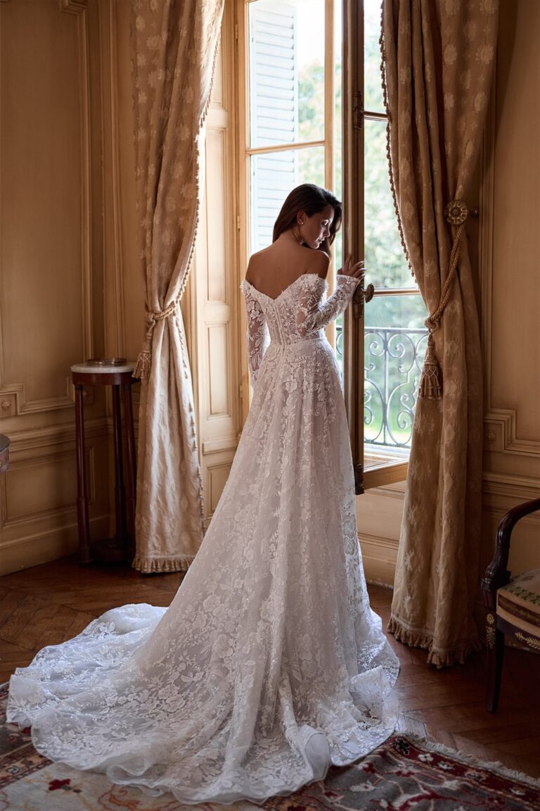 Brautkleid mit langen Spitzenärmeln und Schleppe vor einem Fenster